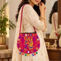 A woman in a cream dress wears a vibrant pink sling bag with embroidered dancers and small mirrors.