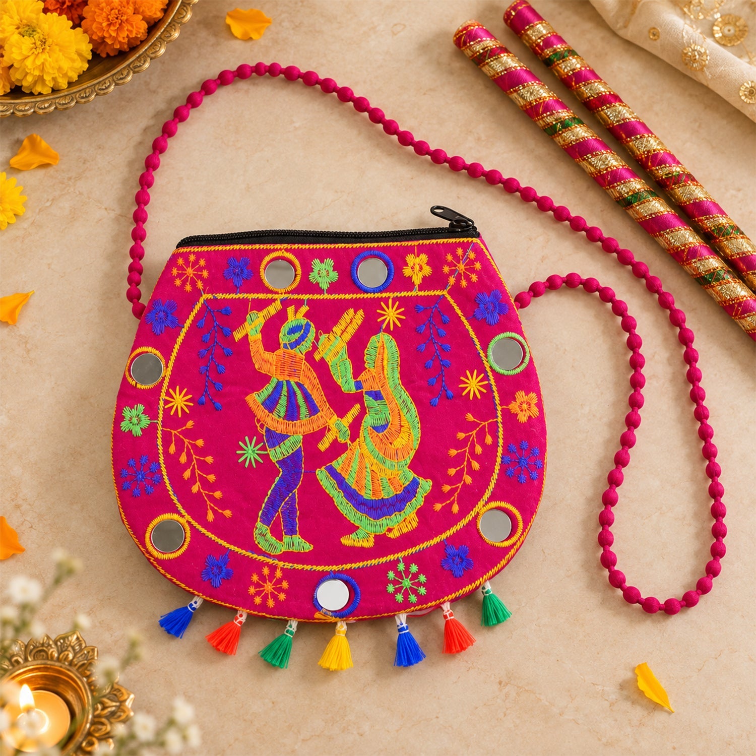 A pink sling bag with embroidered dancing figures, mirrors, and colorful tassels rests on a wooden surface.