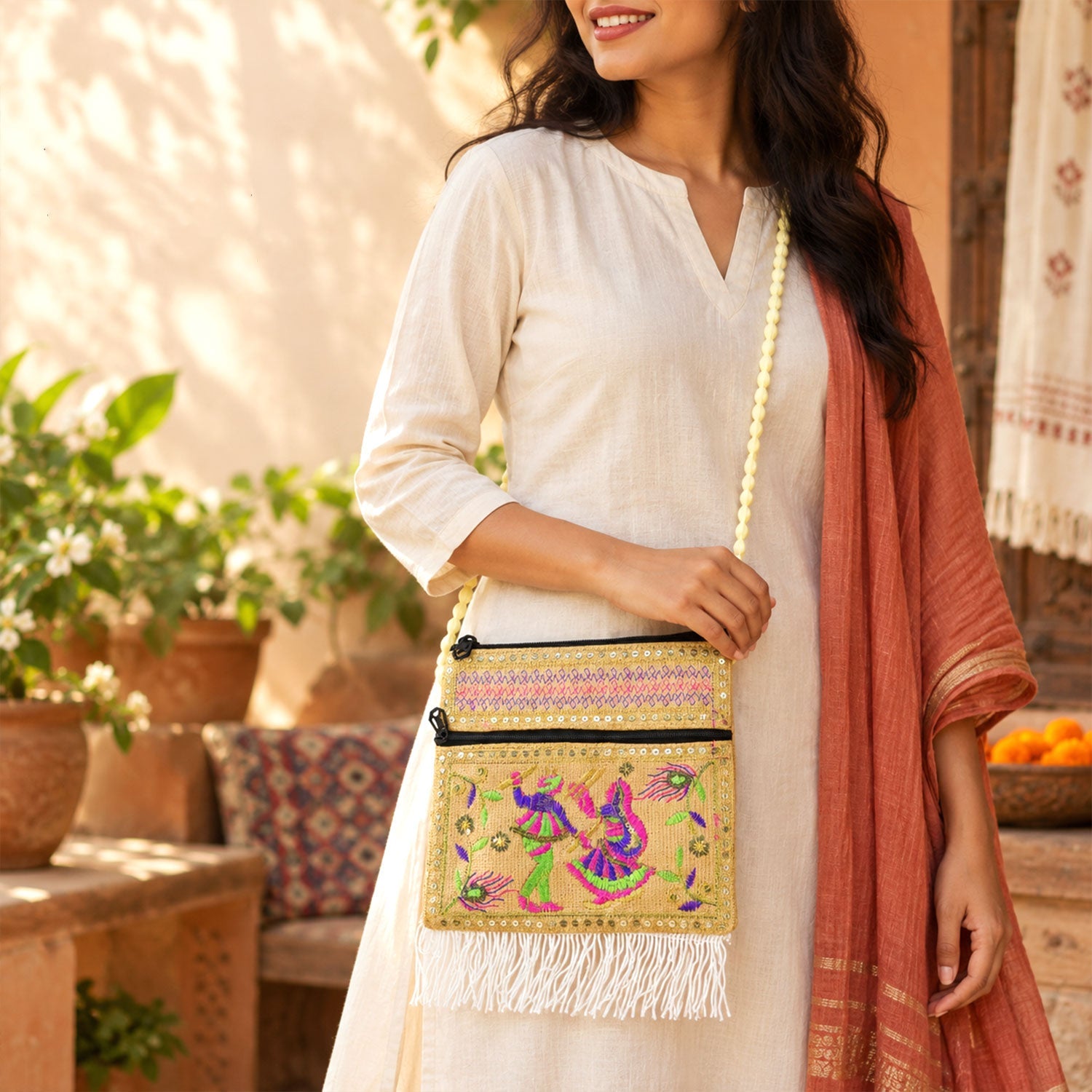 A woman wears a beige embroidered jute sling bag with a long beaded strap and white fringe.