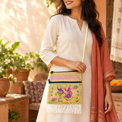 A woman wears a beige embroidered jute sling bag with a long beaded strap and white fringe.