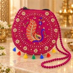 A fuchsia round purse with intricate peacock embroidery and vibrant tassels sits on a marble surface.