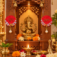 Two red Shubh Labh decorations with pearl drops hang on a carved wooden temple, flanking a golden Ganesha idol surrounded by