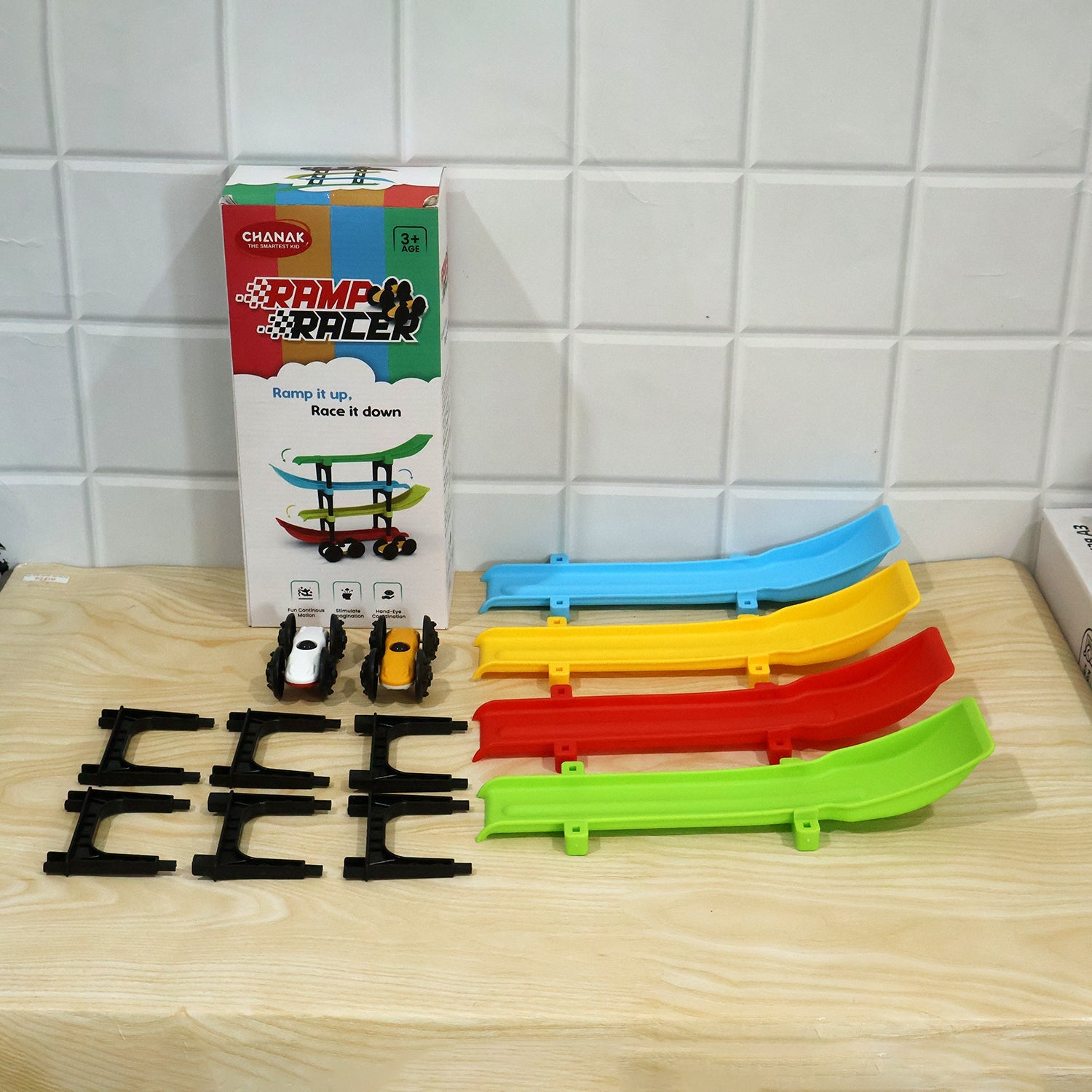 All components of the ramp racer toy set, including the box, ramps, cars, and connectors, arranged on a wooden surface.