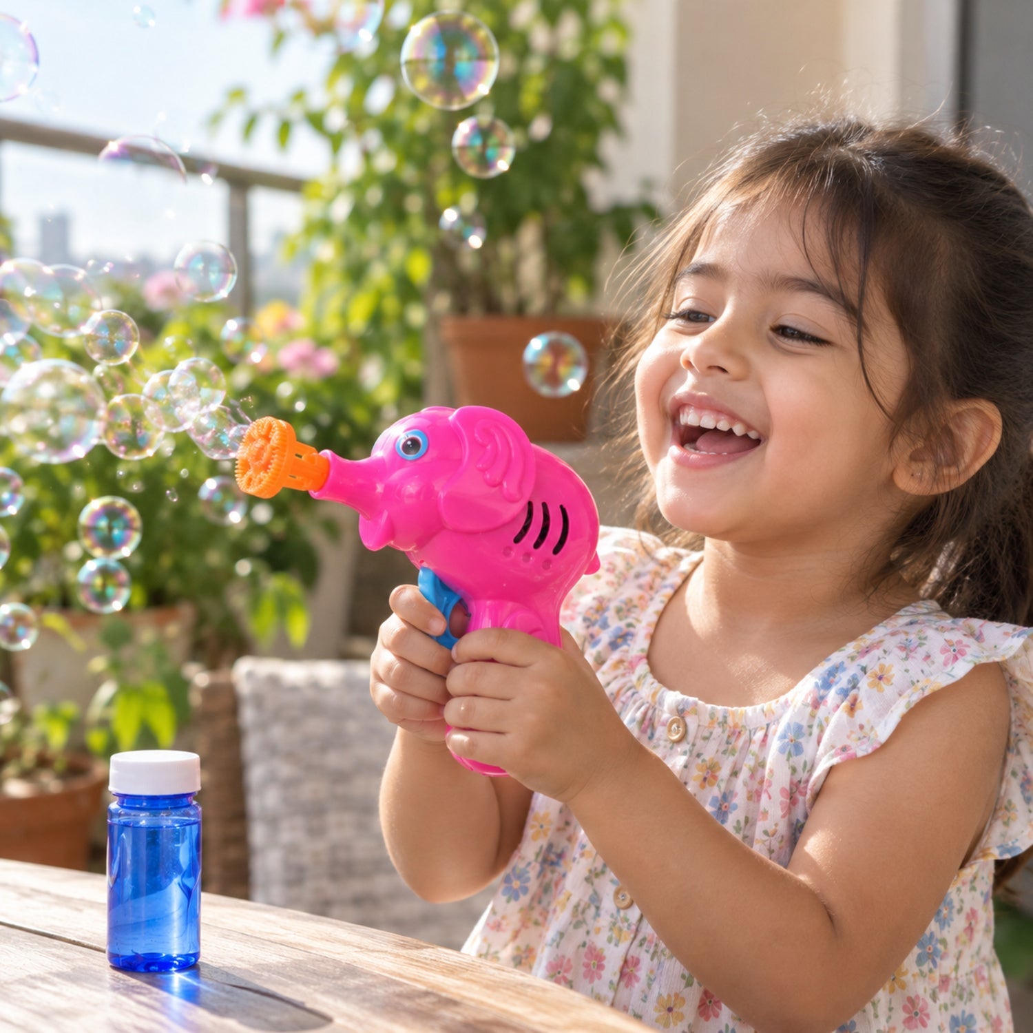 A joyful child holds a pink elephant bubble gun, blowing bubbles outdoors on a sunny patio.