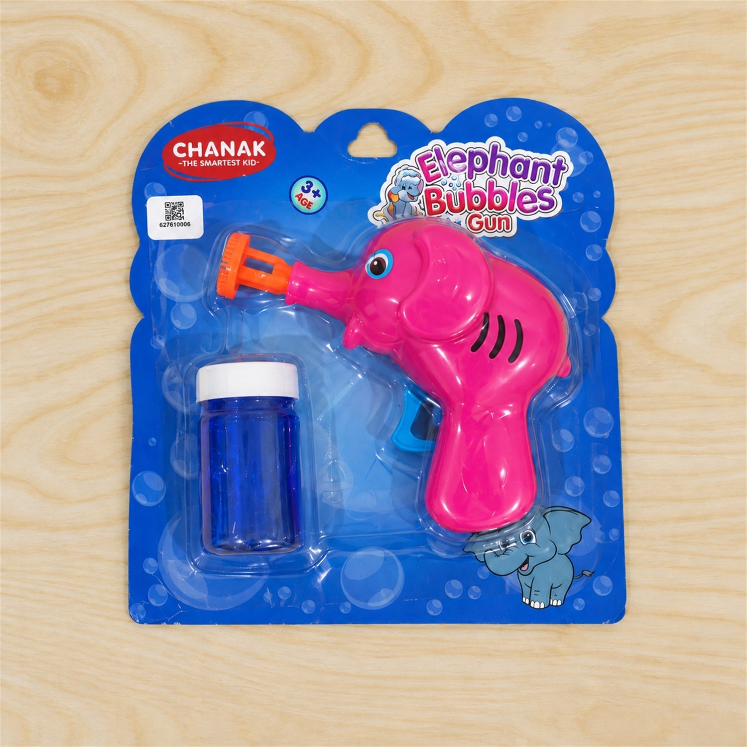 A pink elephant bubble gun and blue solution bottle are sealed in clear plastic packaging on a wooden surface.