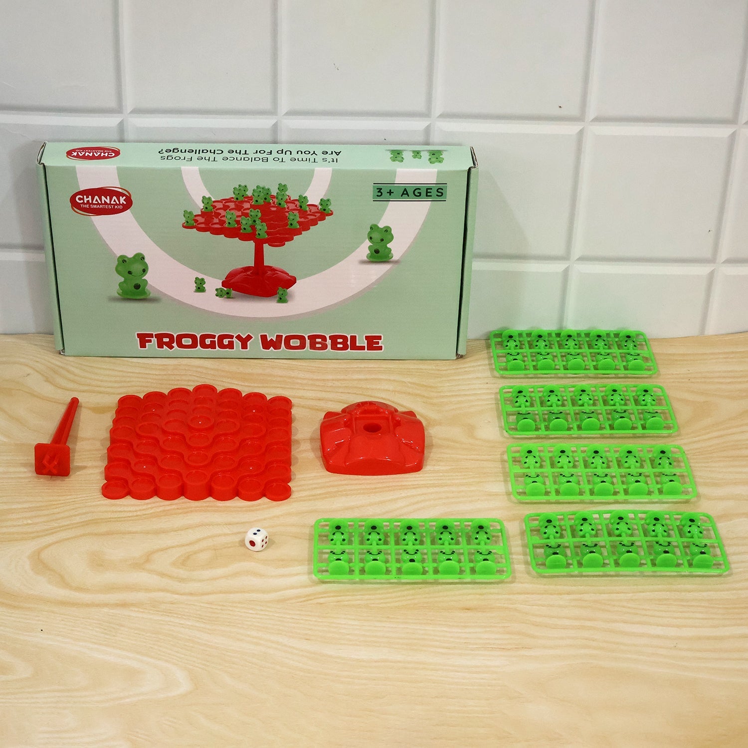 All game components laid out on a wooden table: the product box, red balancing board, base, stand, dice, and multiple trays