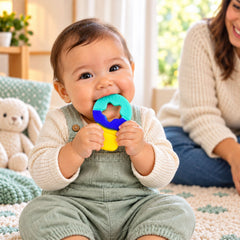 A happy baby in overalls chews on a colorful star-shaped teether with a parent smiling in the background.