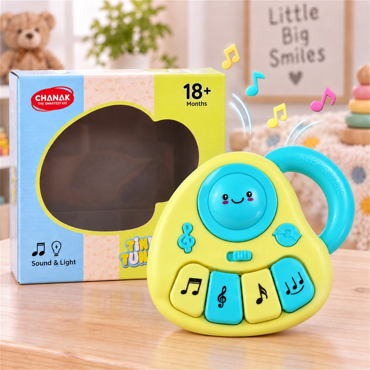 Yellow and blue musical toy with four keys and a handle, next to its packaging on a wooden surface.