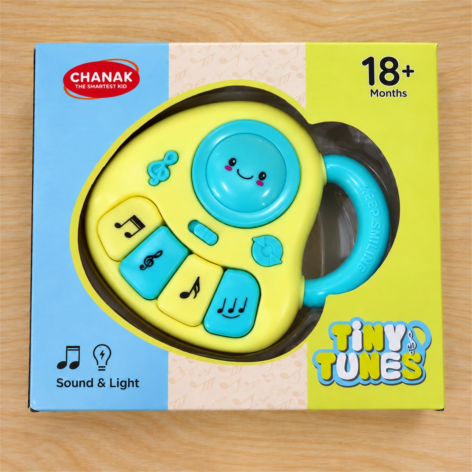 The yellow and blue musical toy is displayed inside its blue and yellow retail box on a wooden surface.