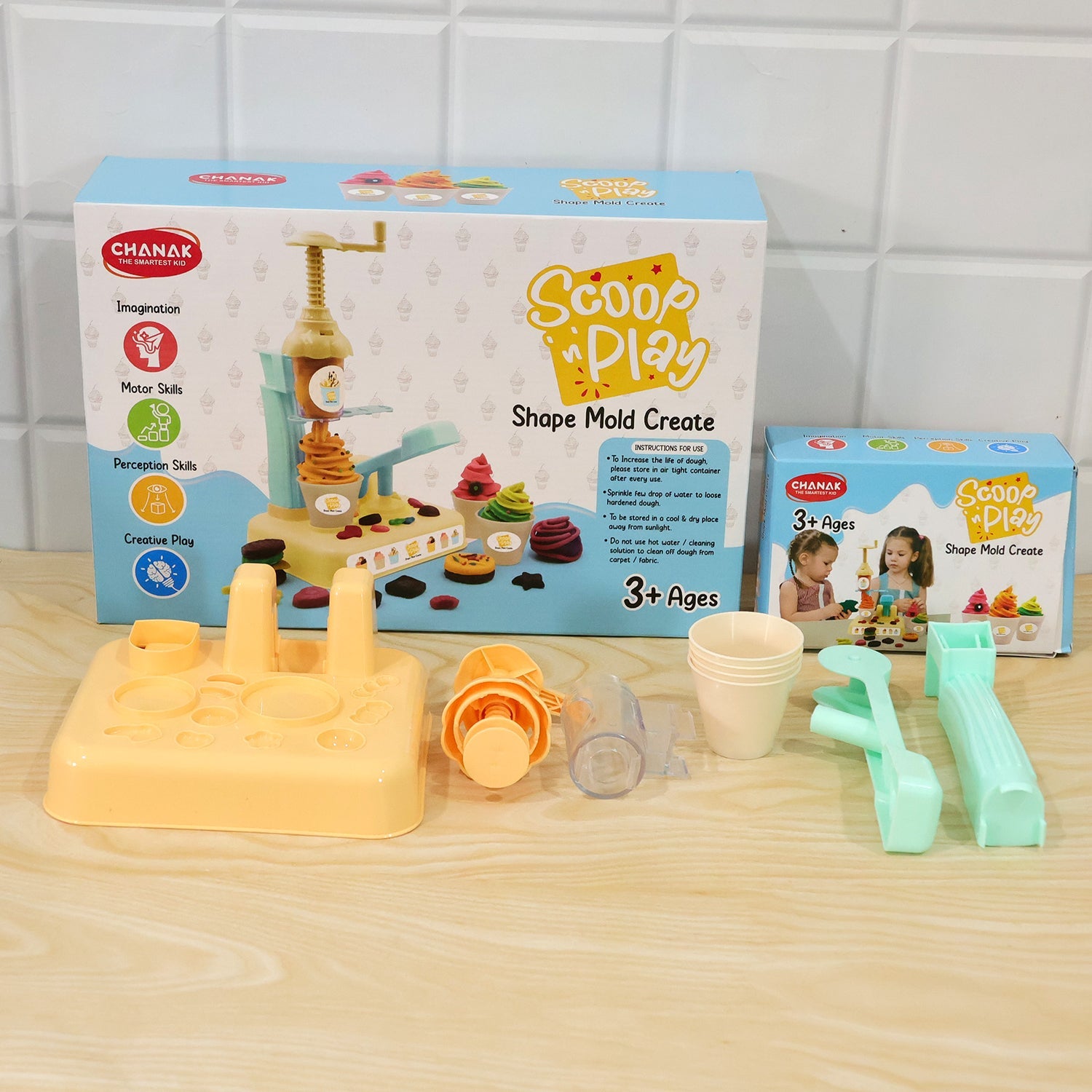The dough ice cream maker play set components laid out next to its product box and a smaller box on a wooden table.