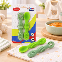 Two green silicone baby spoons, one with a regular spoon head and one with a flower-shaped teether, in clear packaging on a