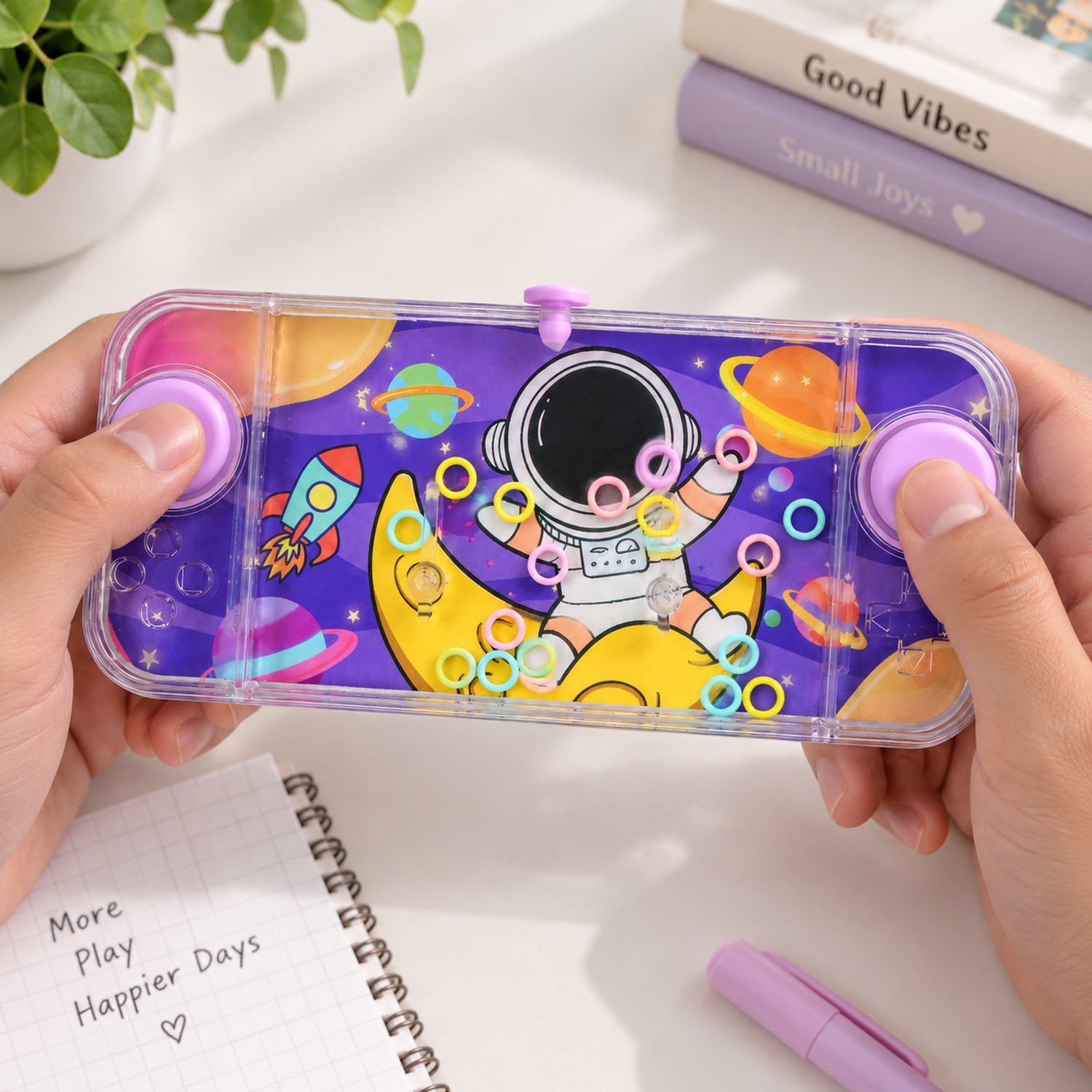A child's hands manipulate the purple water game, attempting to loop colorful rings onto the small posts.
