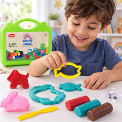 A boy smiles while holding a brown clay fish, with a green case, colorful clay, and plastic moulds on the table.
