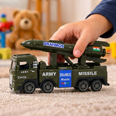 A child's hand pushes a green toy army truck with a missile launcher across a textured surface.