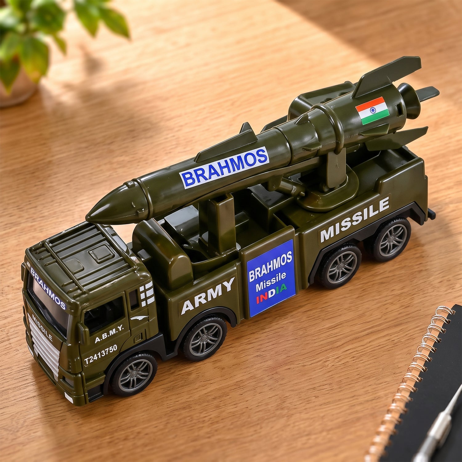 A green toy army truck with a missile launcher on its back sits on a wooden table next to a notebook.