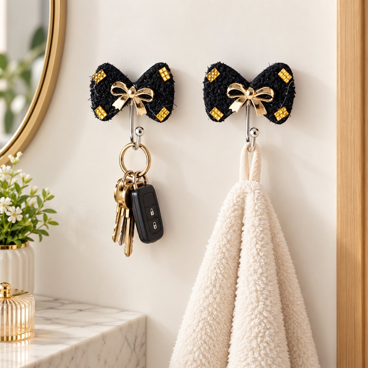 Two black bow-shaped hooks mounted on a wall, one holding a set of keys and the other a cream-colored towel.