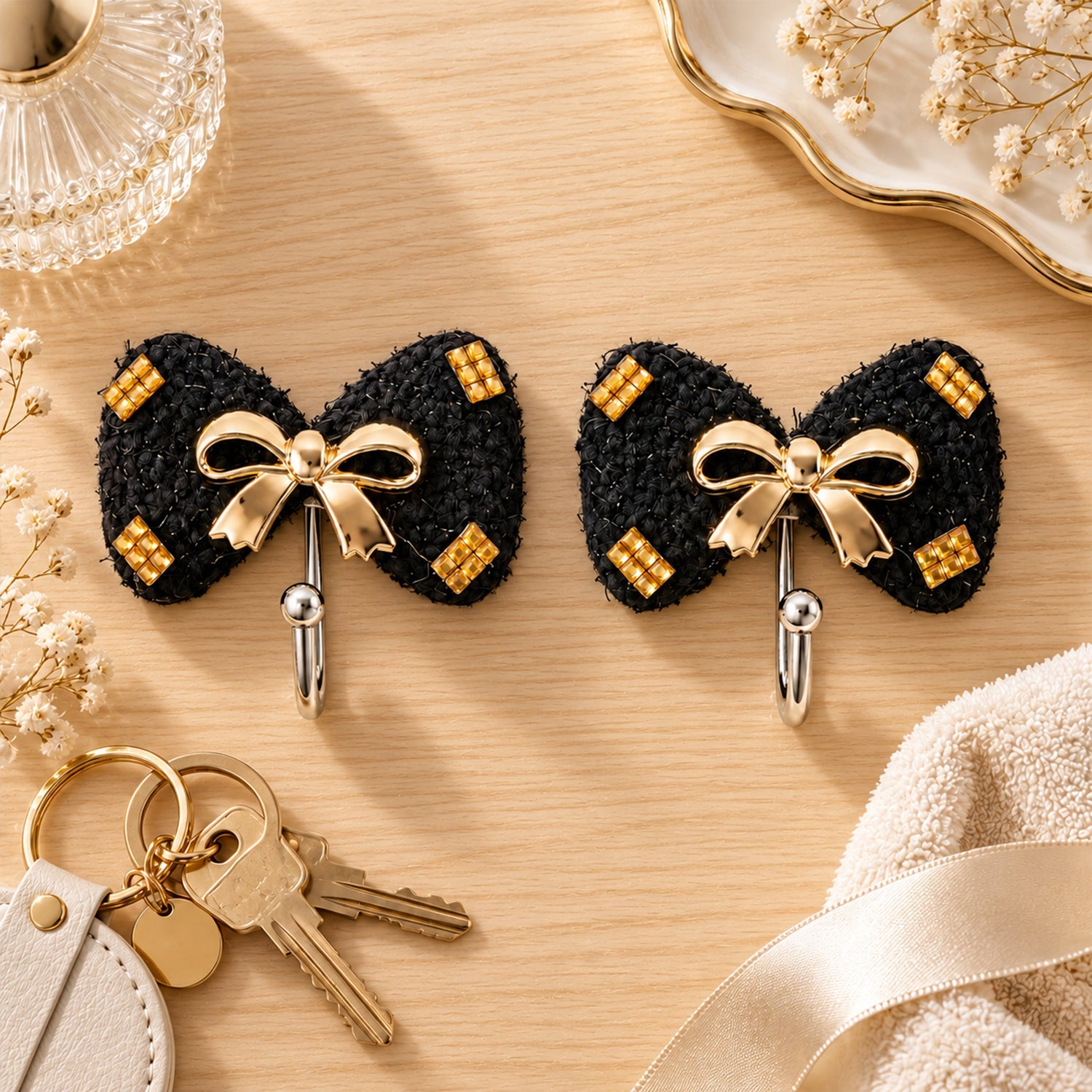 Two black bow-shaped hooks with gold accents on a wooden surface, next to a set of keys and a folded cream towel.