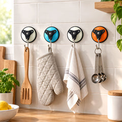 Four colorful suction cup hooks on a white tiled kitchen wall, holding a wooden spatula, an oven mitt, a white towel, and
