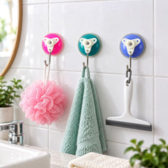 Three vibrant suction cup hooks in pink, teal, and blue, holding a pink loofah, a green towel, and a white squeegee on a