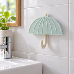 Pastel green umbrella hook mounted on white tiled bathroom wall above a sink faucet.