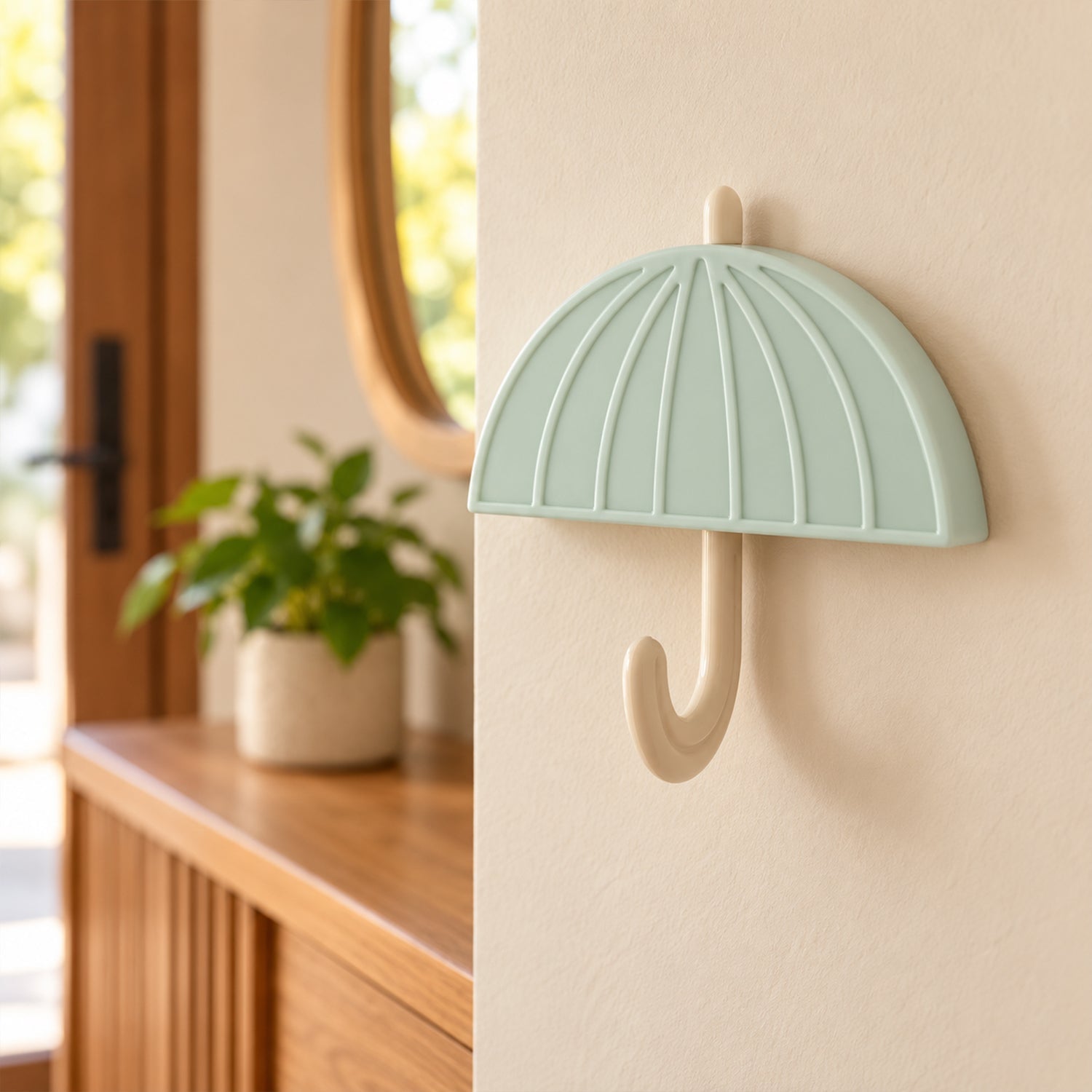 Side view of the light green umbrella hook on a beige wall, with a wooden console table and mirror in background.