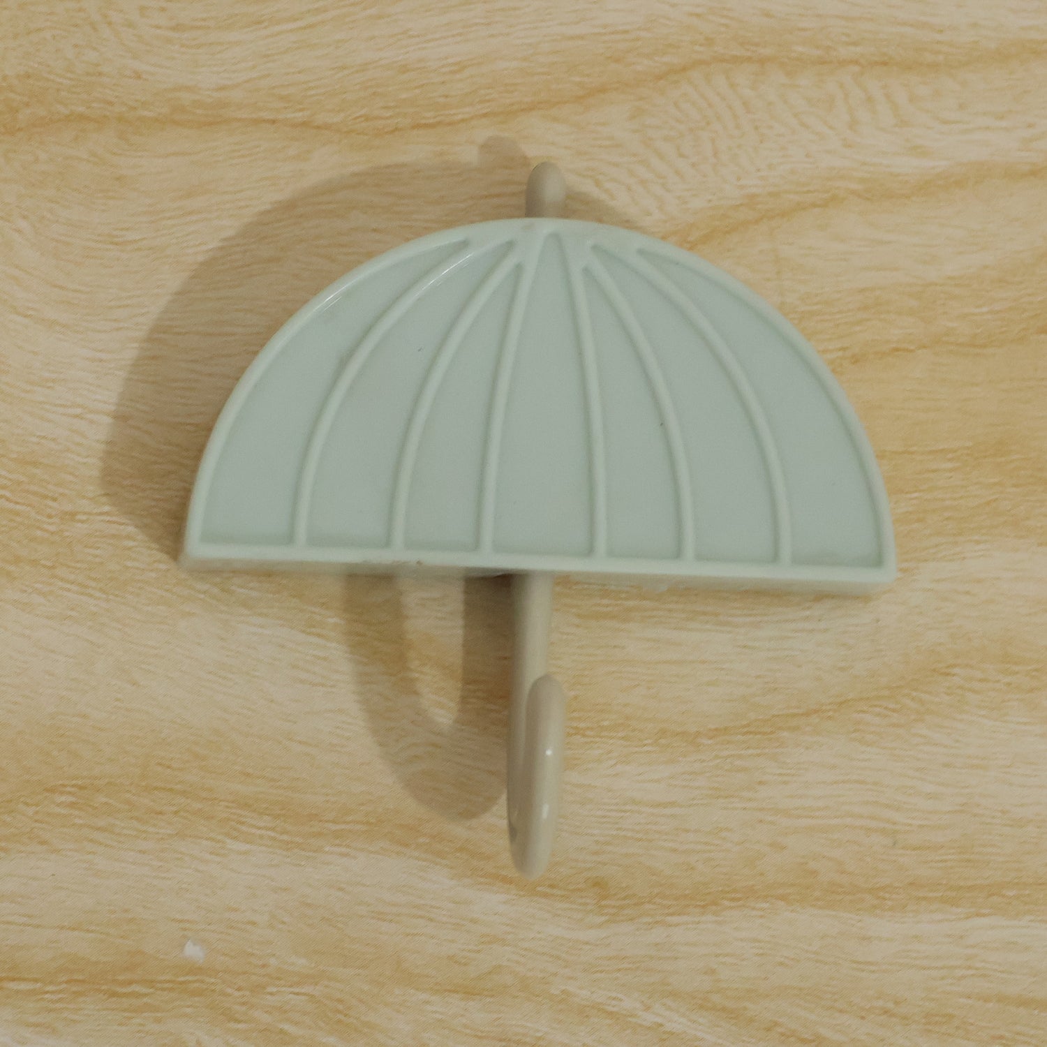 Close-up, top-down view of the umbrella-shaped hook mounted on a light brown wooden surface.