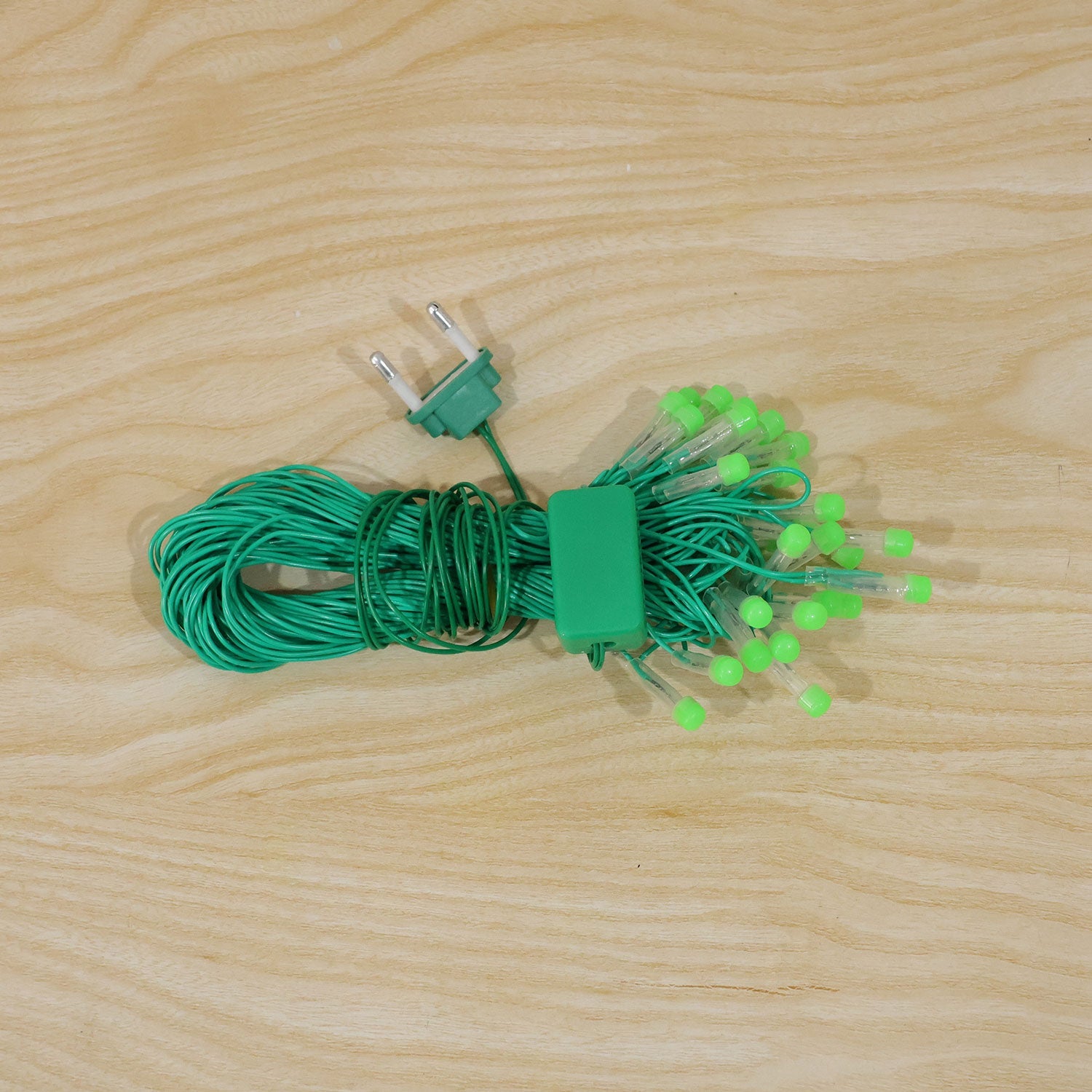 A coiled bundle of green LED string lights with a 2-pin plug and controller resting on a wooden surface.
