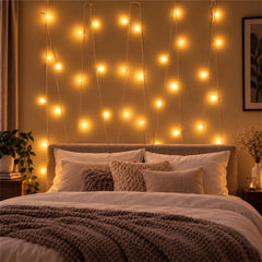 A bedroom wall adorned with vertical strands of warm yellow LED string lights above a bed with pillows and a blanket.