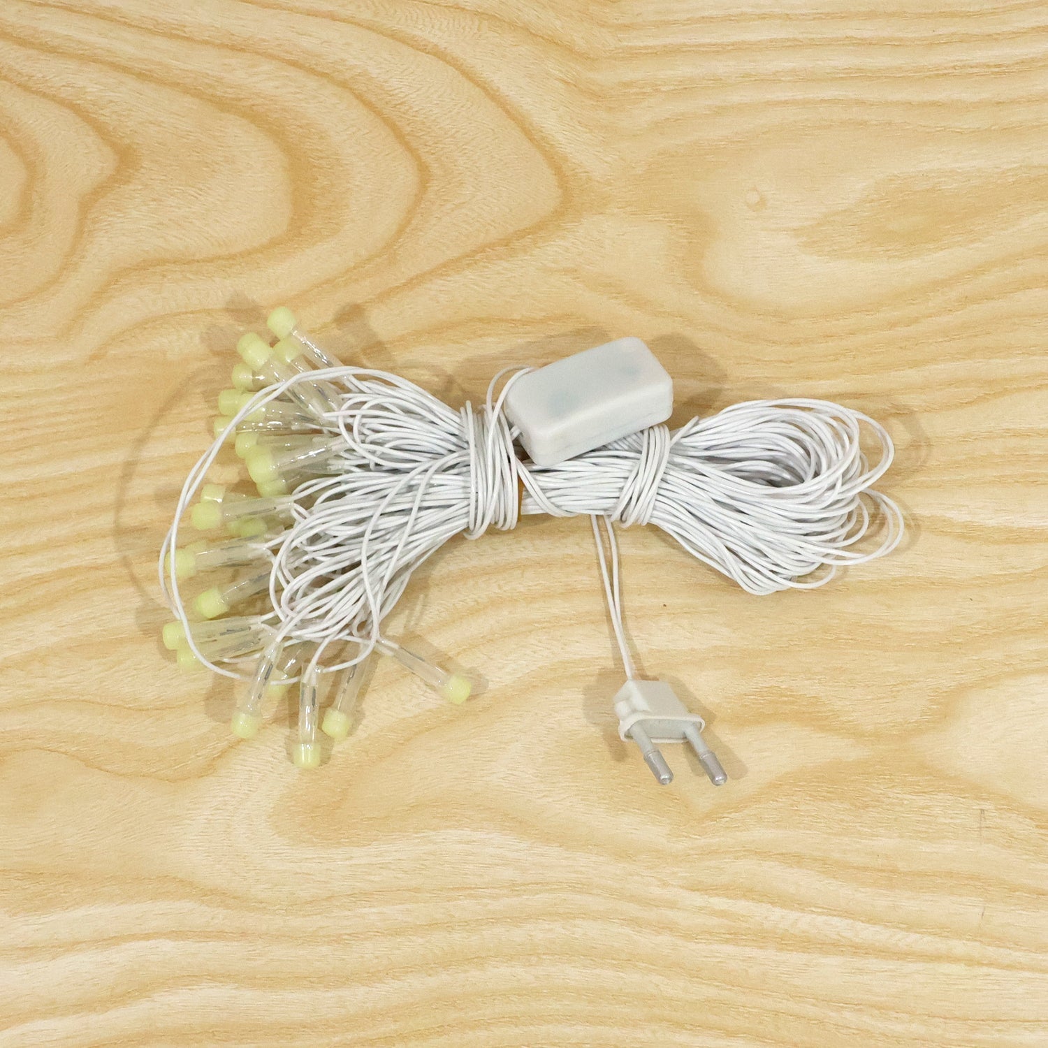 A coiled white LED string light set with clear bulbs and a power adapter, displayed on a light wooden surface.