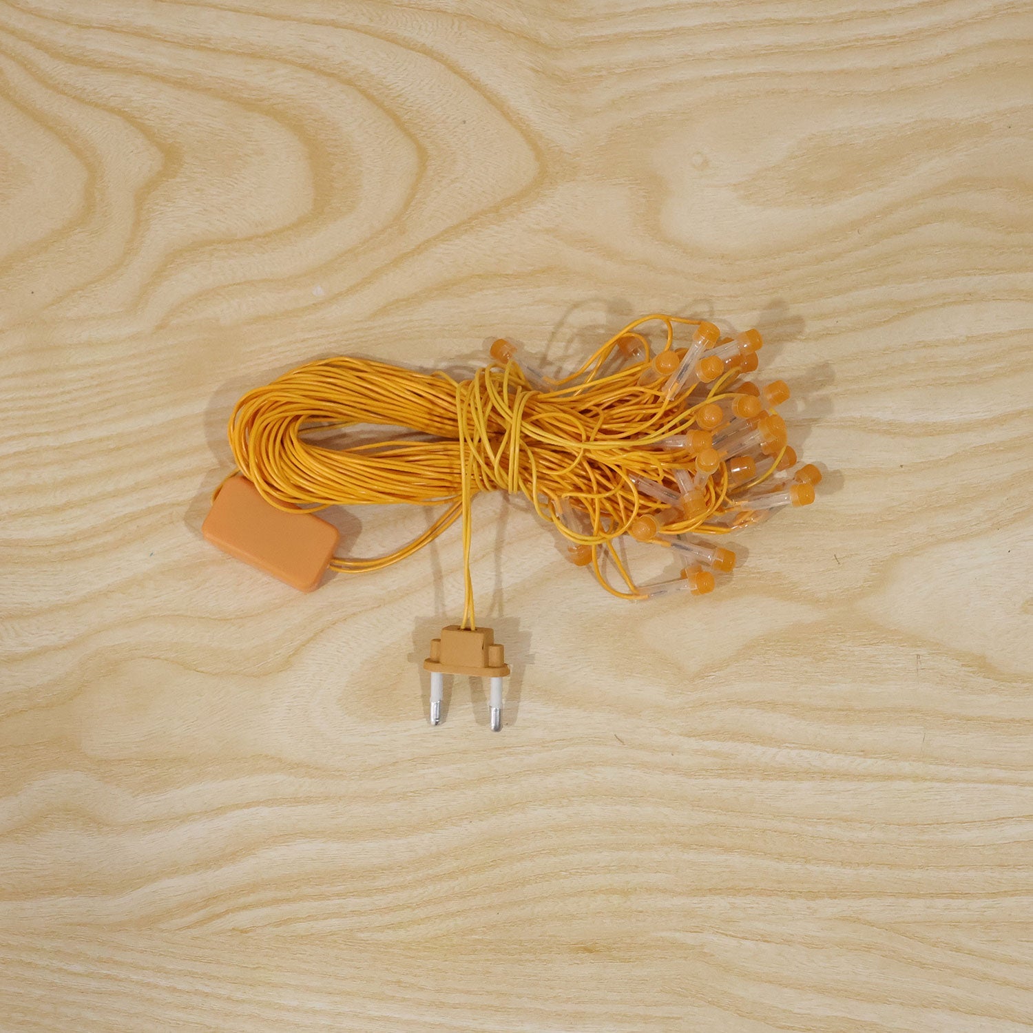 A coiled bundle of orange LED curtain lights with a plug and control box rests on a wooden surface.