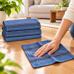 A hand wipes a wooden floor with a blue cloth, three folded cloths are stacked beside it.