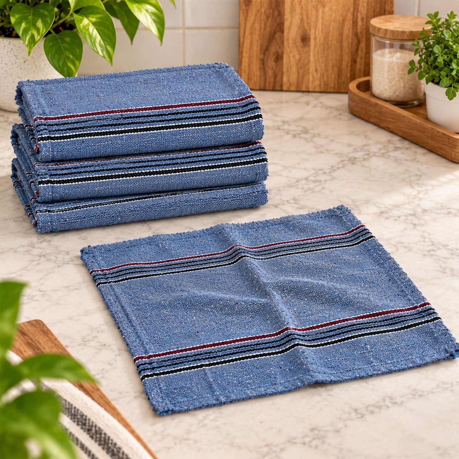 Four blue woven cloths with striped borders, one unfolded on a counter, three stacked nearby.