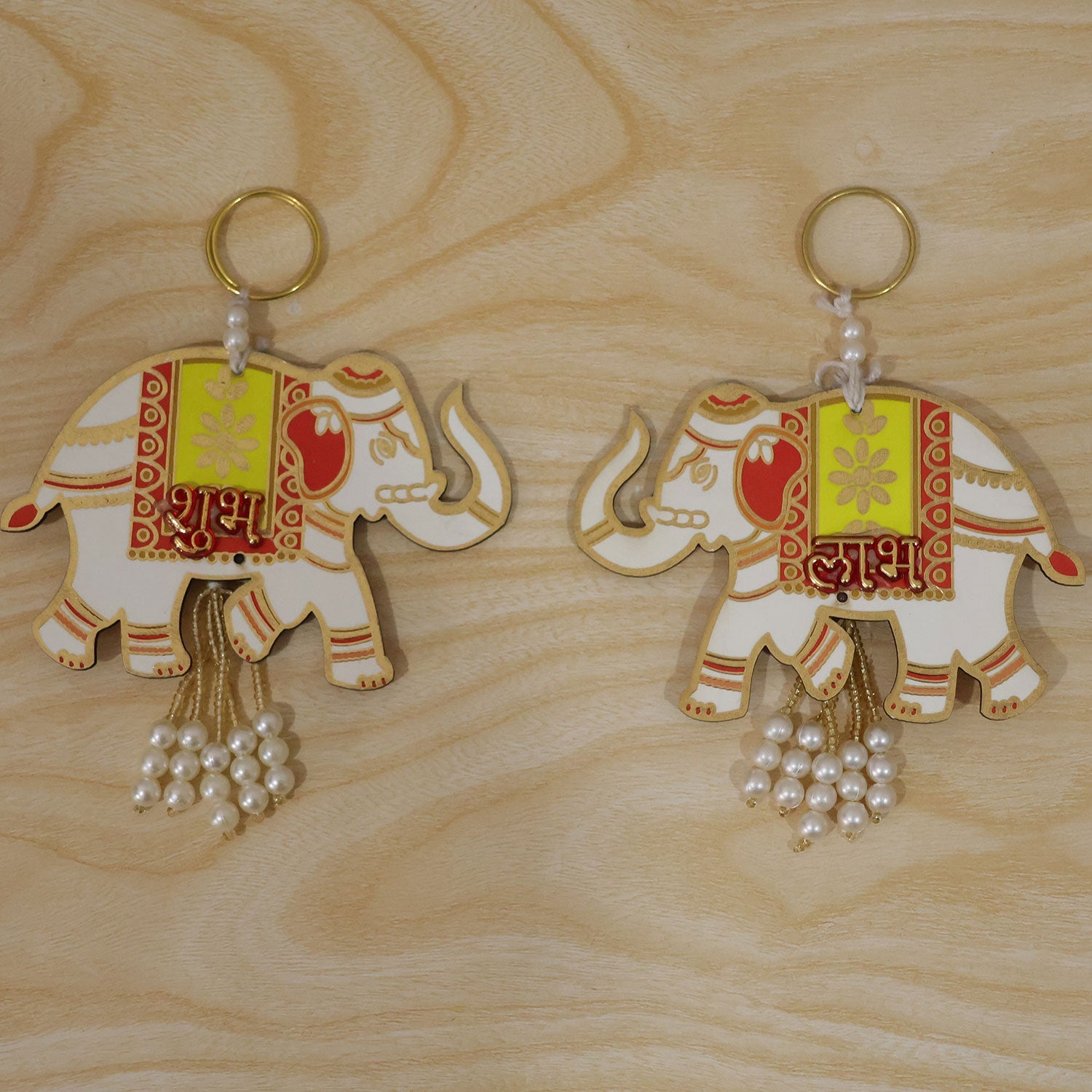 A pair of white and yellow elephant hangings with red accents and pearl tassels lie on a light wood surface.