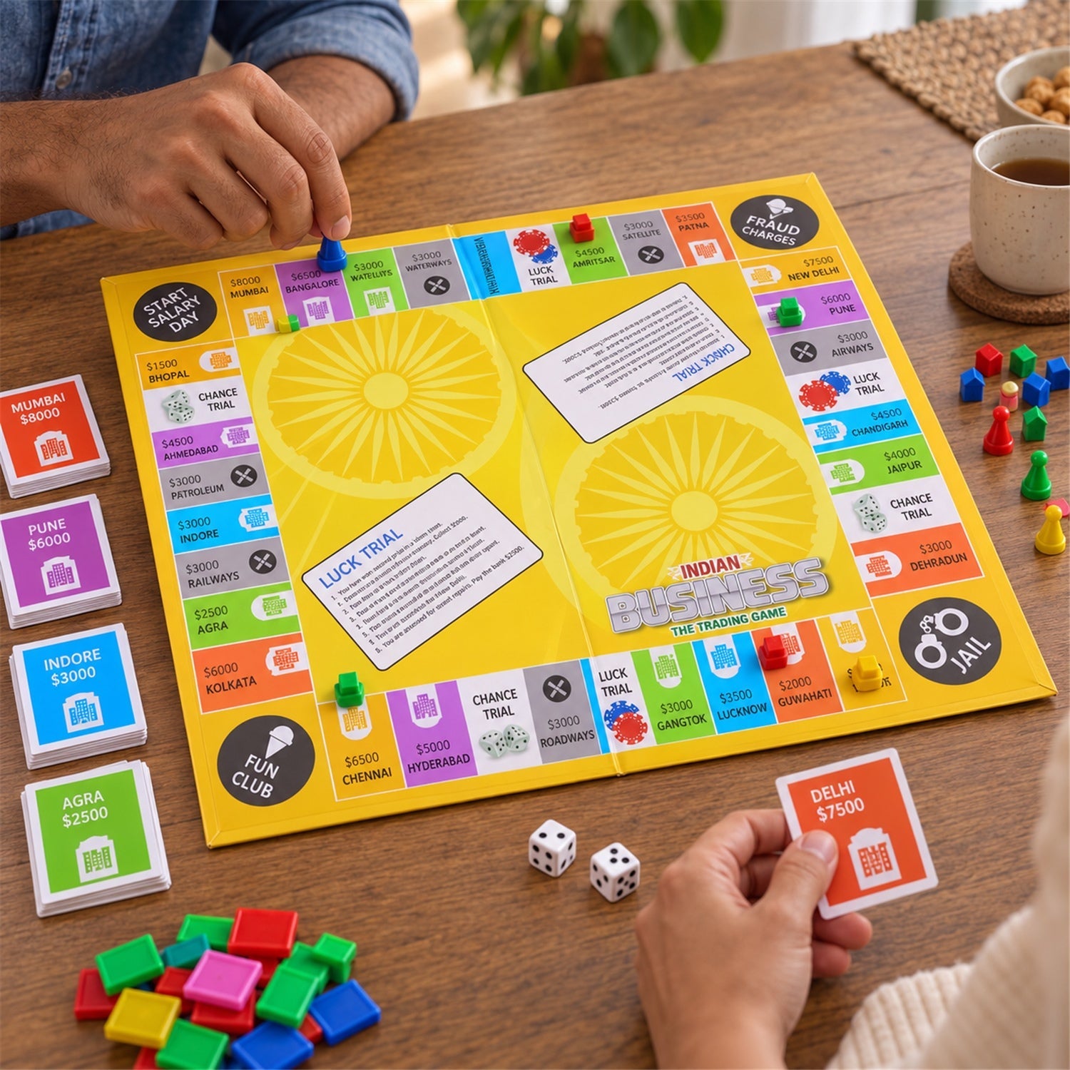 Two people's hands interact with the yellow Indian Business game board, colorful pieces, and dice on a wooden surface.
