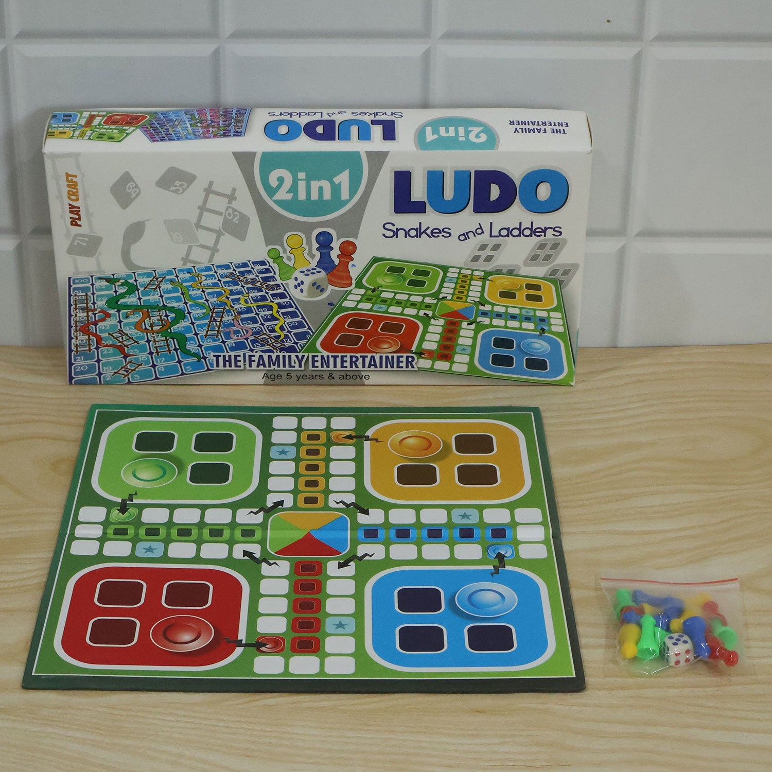 The Ludo and Snakes and Ladders game box, open board, and a small bag of game pieces on a white tiled surface.