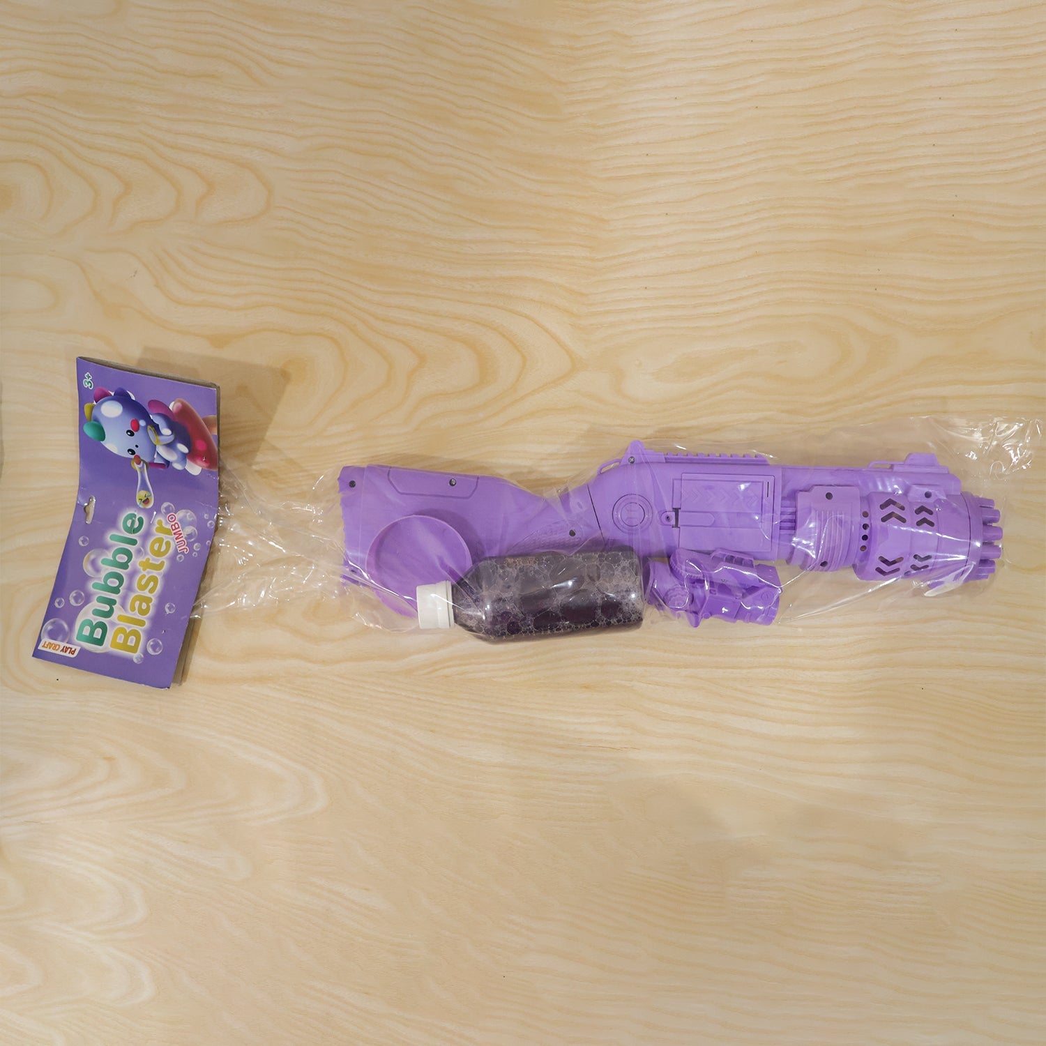 A purple bubble gun and a small bottle of solution are sealed in clear plastic packaging next to a purple instruction card