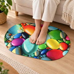 Bare feet standing on an oval mat with a vibrant, glossy pebble pattern in various bright colors.