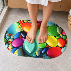 Bare legs and feet standing on a colorful oval pebble-patterned mat on a light grey tiled floor.