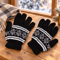 Pair of black knitted gloves with white and gray snowflake pattern on a wooden table with a plaid blanket.