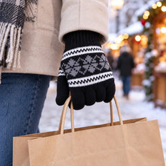 Person wearing a black knitted glove with a snowflake design, carrying a brown paper shopping bag outdoors.