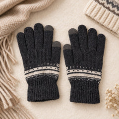A pair of dark gray knitted gloves with white patterned cuffs lies flat on a light surface beside a beige scarf and hat.