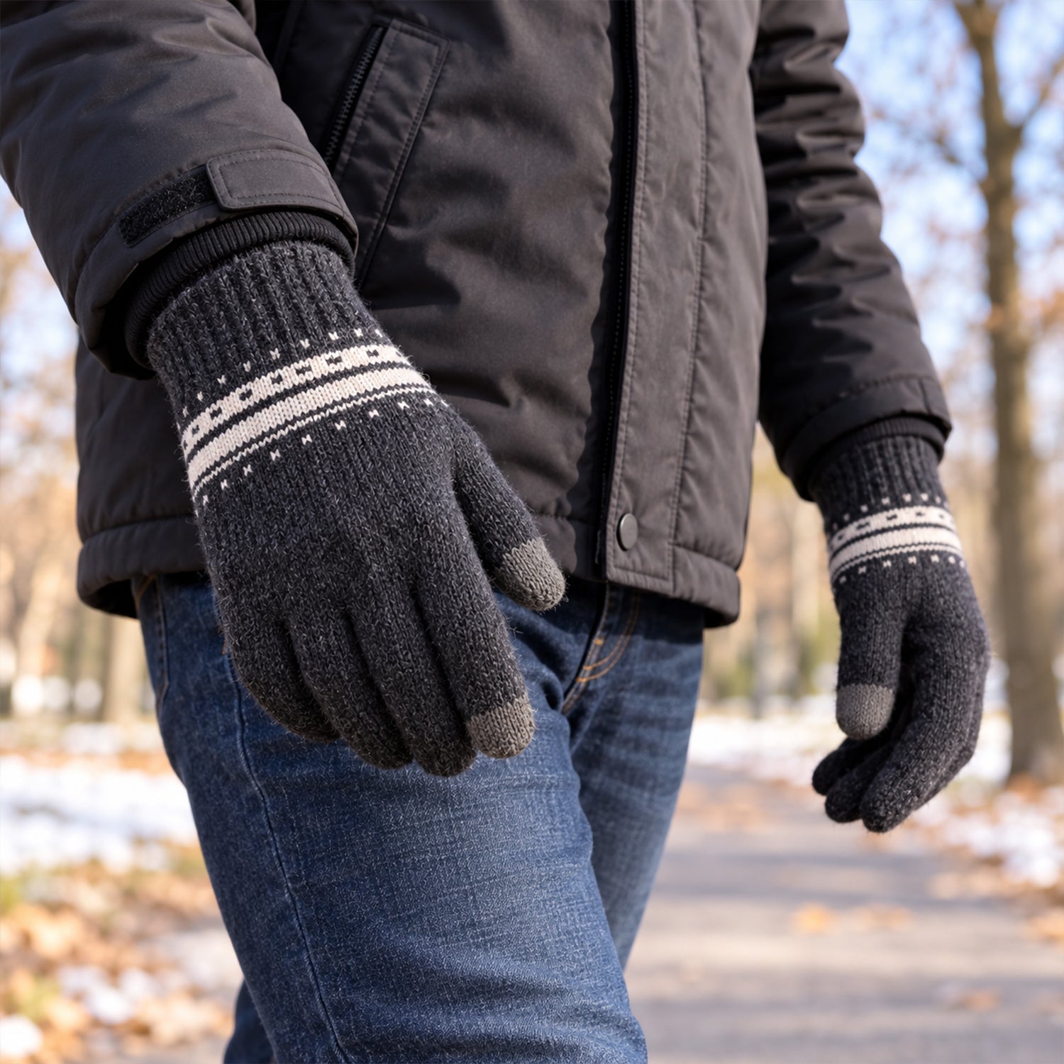 A person wearing a dark jacket and jeans walks outdoors in dark gray knitted gloves with white patterned cuffs.