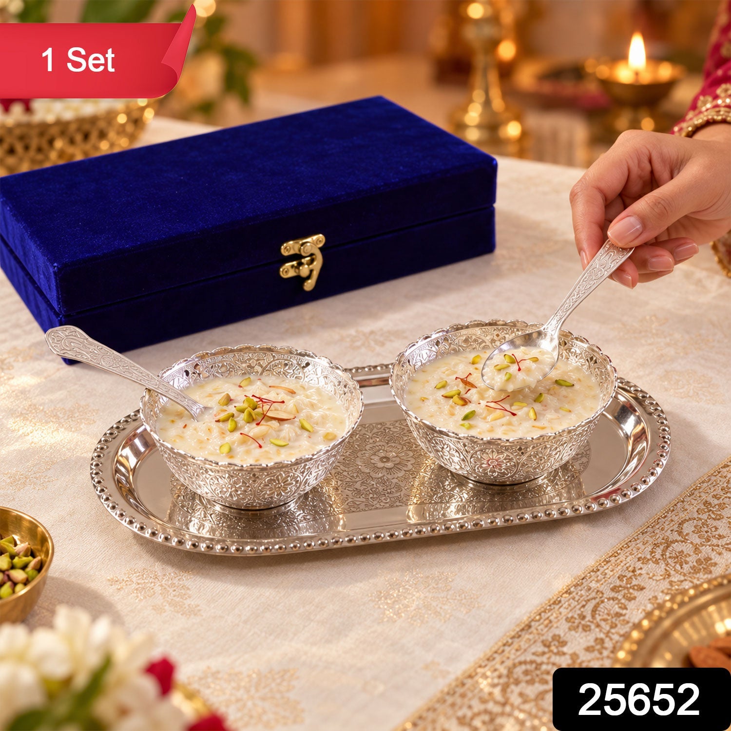 A hand holds a silver spoon above a bowl of dessert on an ornate silver tray, next to a blue velvet box. â€“ view 2