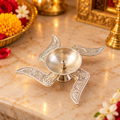 An ornate silver swastik diya with a central oil holder is placed on a light brown marble surface.