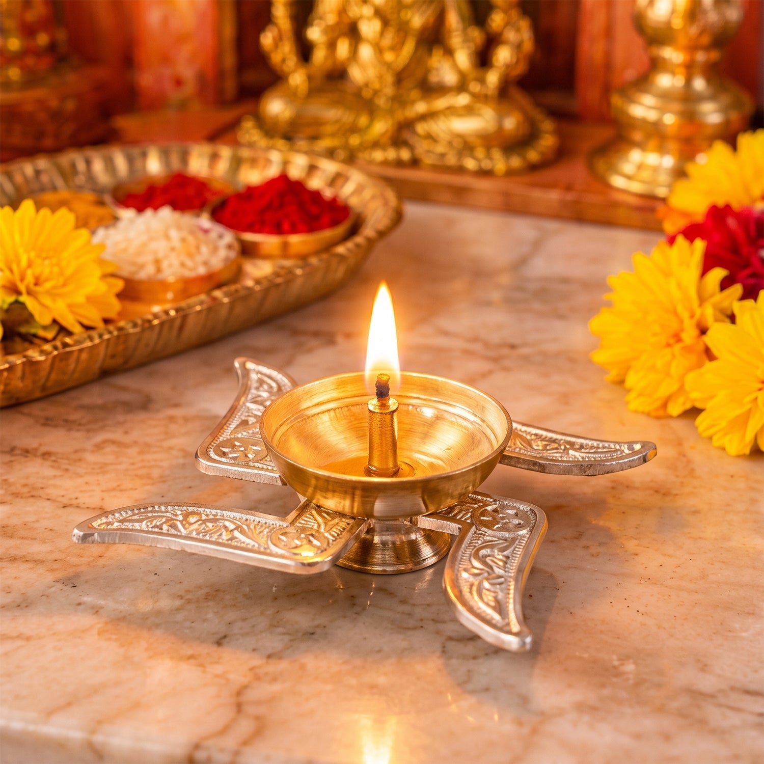 A lit silver and brass swastik diya illuminates a marble surface, with a blurred golden tray in the background.