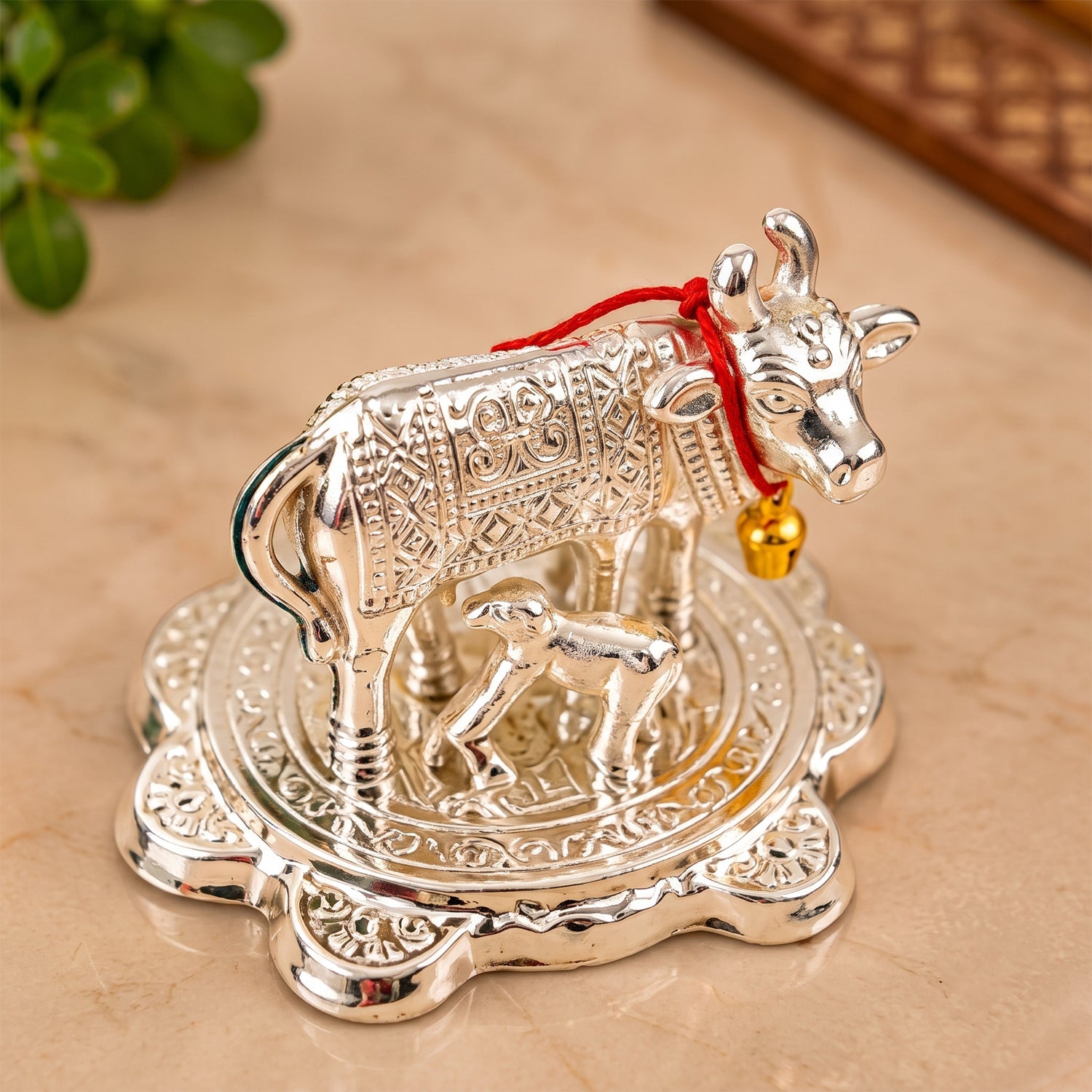 An angled shot of the silver Kamdhenu cow and calf idol on a light marble surface.