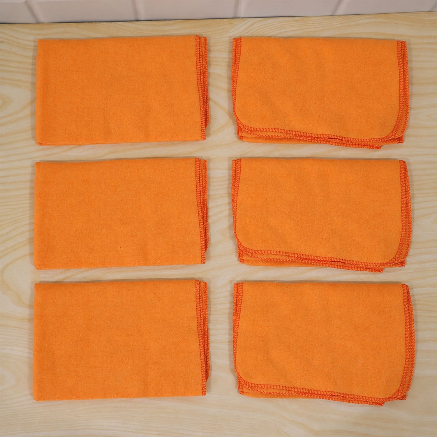Six orange microfiber cloths, some folded, some flat, neatly arranged on a light wooden surface.