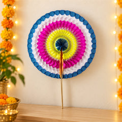 A vibrant paper hand fan with concentric circles of blue, white, pink, yellow, and dark blue, standing upright on a wooden