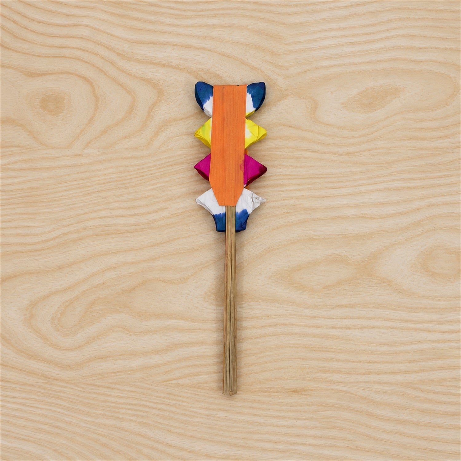 A folded paper hand fan, revealing its compact, layered structure of blue, yellow, pink, and white paper, with a wooden