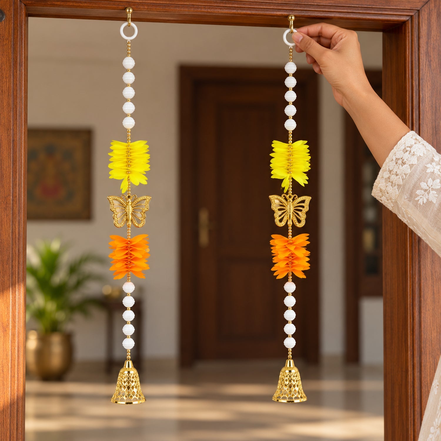 A hand adjusting one of two decorative door hangings, each with yellow and orange paper flowers, a golden butterfly, and a